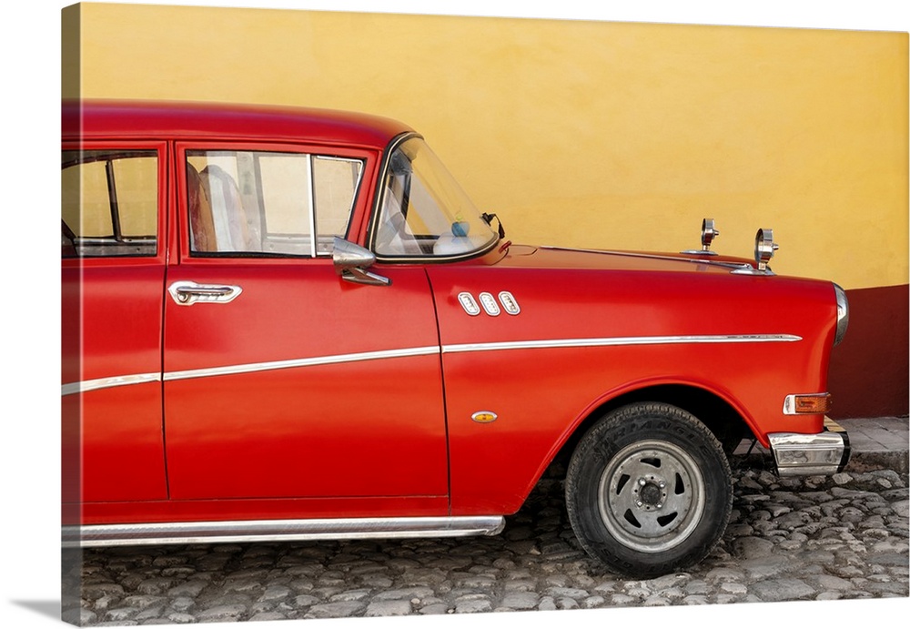 Close-up of Retro Red Car parked on a cobblestone road with a yellow and red wall in the background.