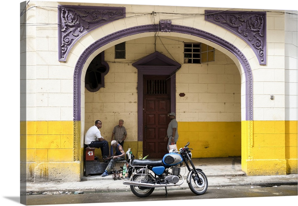 Photograph of a blue motorcycle parked along a street in Havana with pretty purple architectural details in the background.