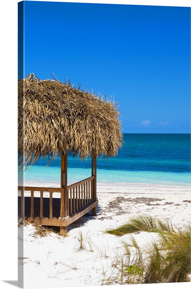 Relaxing photograph of a cabana on the white sands of a Cuban beach with beautiful blue water in the background.