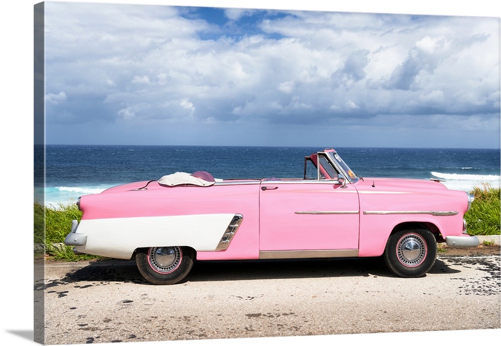 Photograph of a light pink and white vintage convertible parked in front of the ocean.