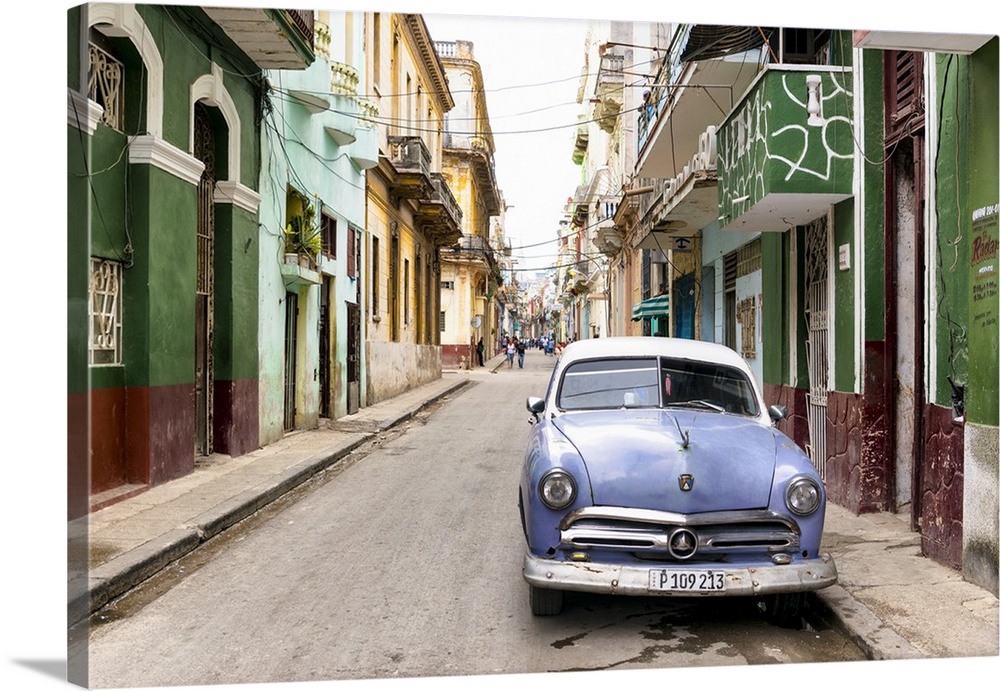 Photograph of a blue vintage Ford car parked in a Havana street surrounded by buildings.