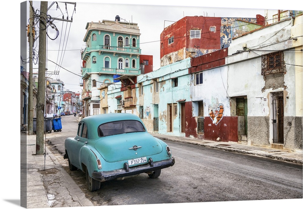 Photograph of a vintage turquoise car parked in the street surrounded by worn buildings in Havana, Cuba
