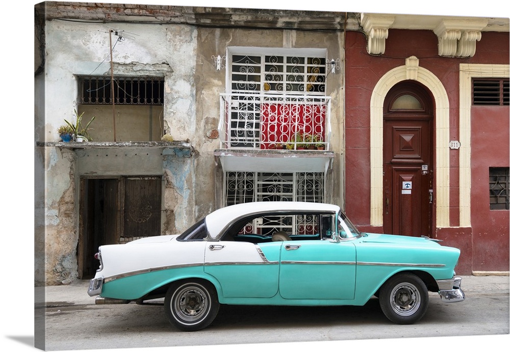 Photograph of a turquoise and white vintage card parked on the side of a street in Havana with weathered buildings in the ...