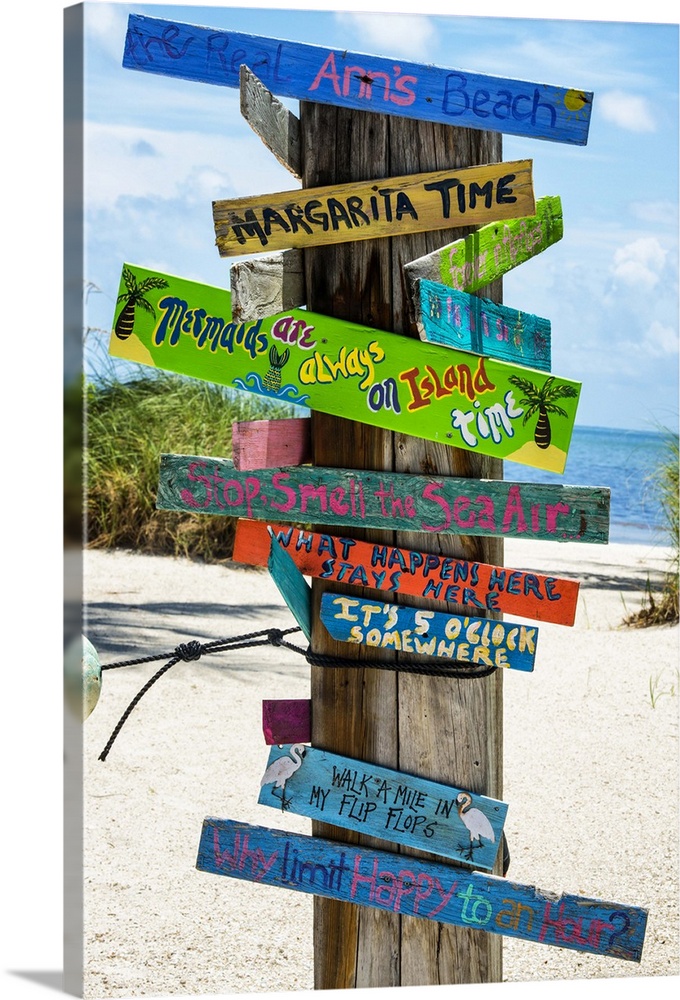 A collection of colorful humorous signs on a wooden post on the beach.