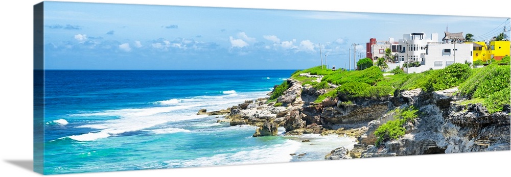 Panoramic photograph of the Isla Mujeres coastline displaying a rocky shore and buildings in the distance. From the Viva M...