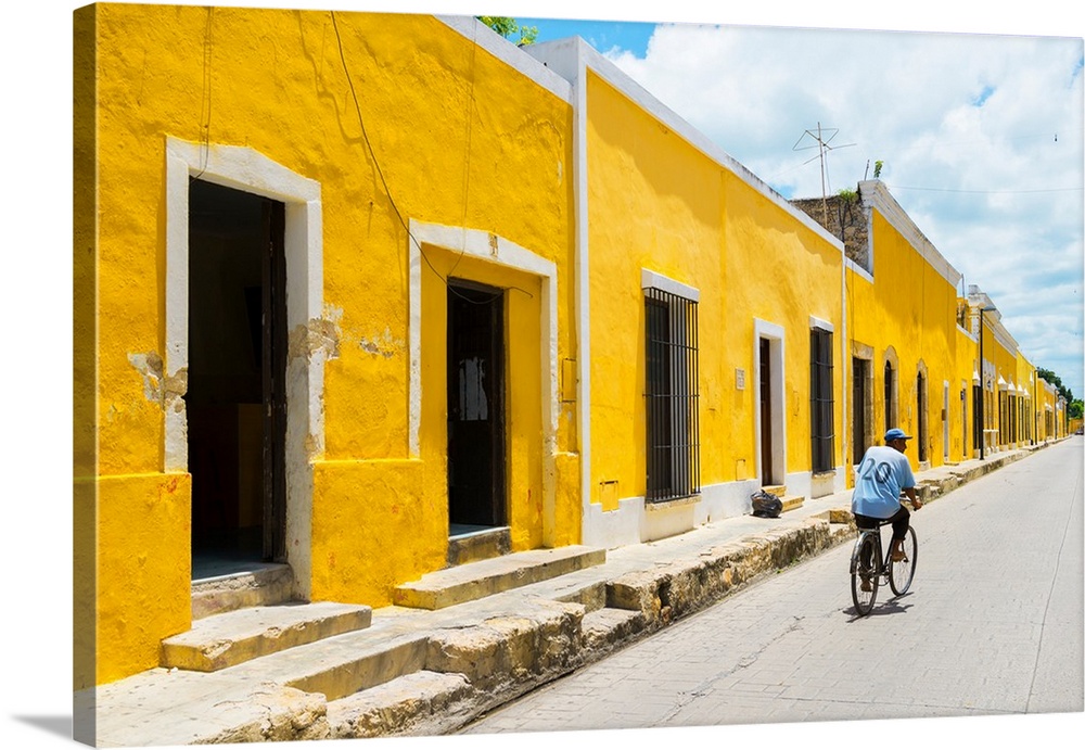 Pphotograph highlighting the yellow buildings in Izamal, Yucat?n, Mexico, with a man in blue riding a bicycle down the roa...