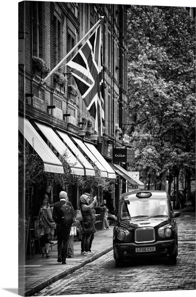 Black and white image of a taxi cab on the street next to awnings in London, England.