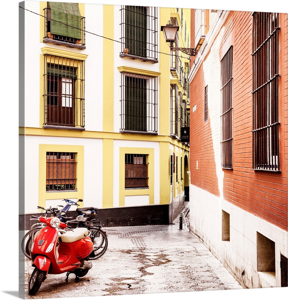 It's a traditional spanish street with colorful facades and a red scooter in the city of Seville in Spain.