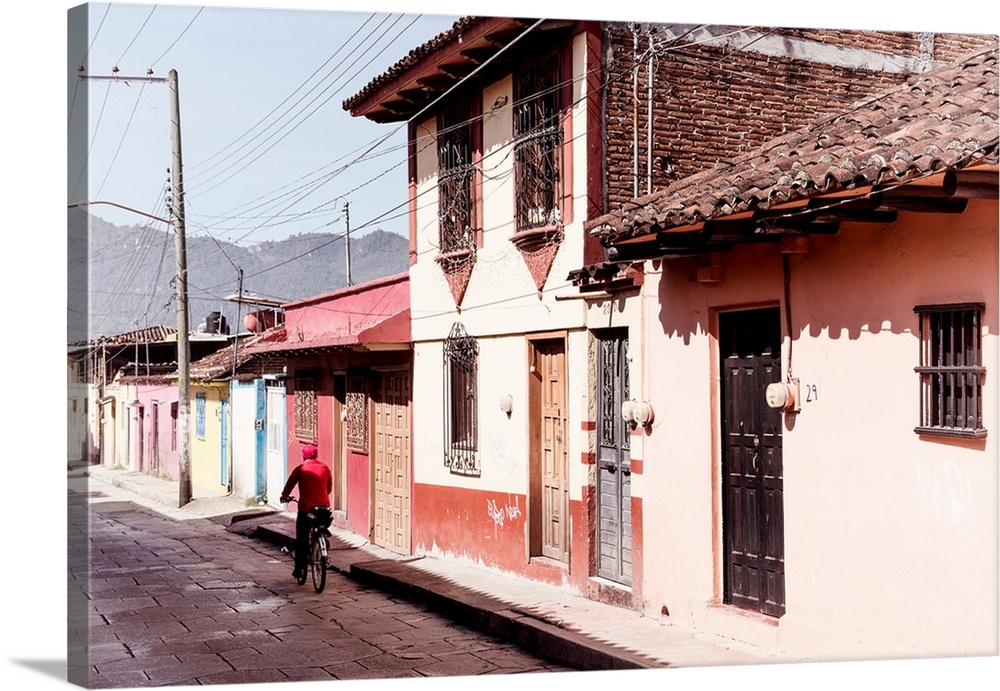 Photograph of a streetscape in Mexico with a man in red riding a bike down the road. From the Viva Mexico Collection.