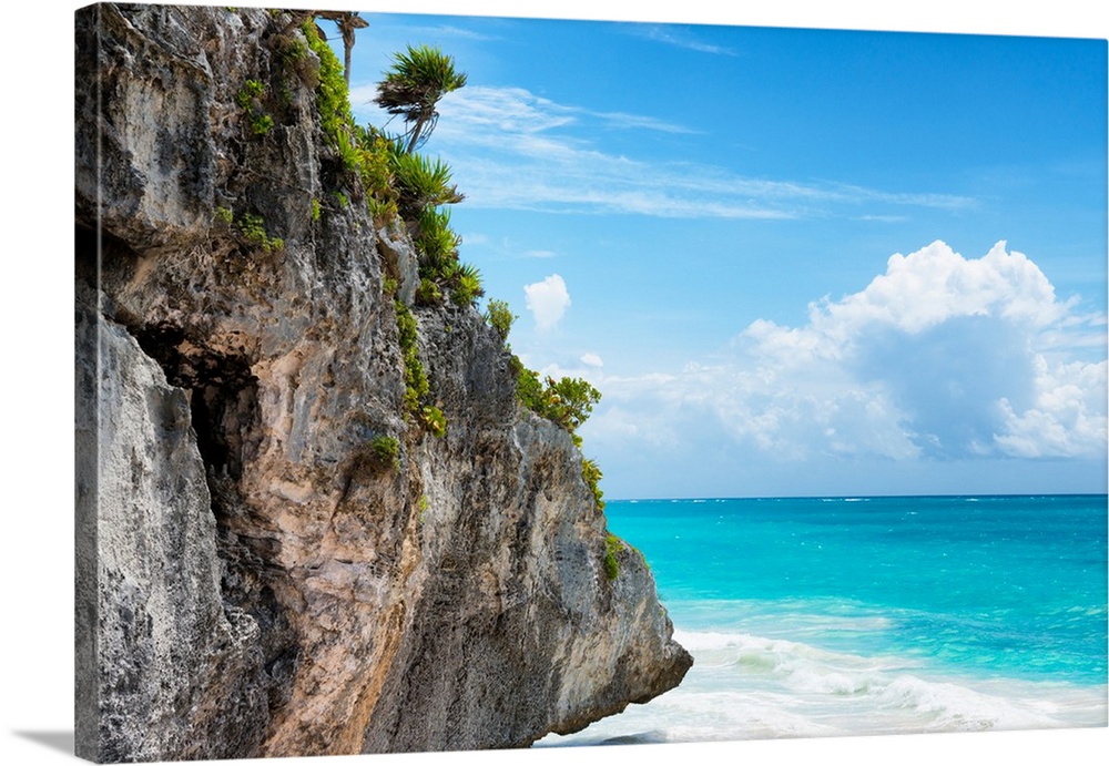 Photograph of a giant rock with tropical vegetation and palm trees hanging over the clear Caribbean ocean on a beautiful d...