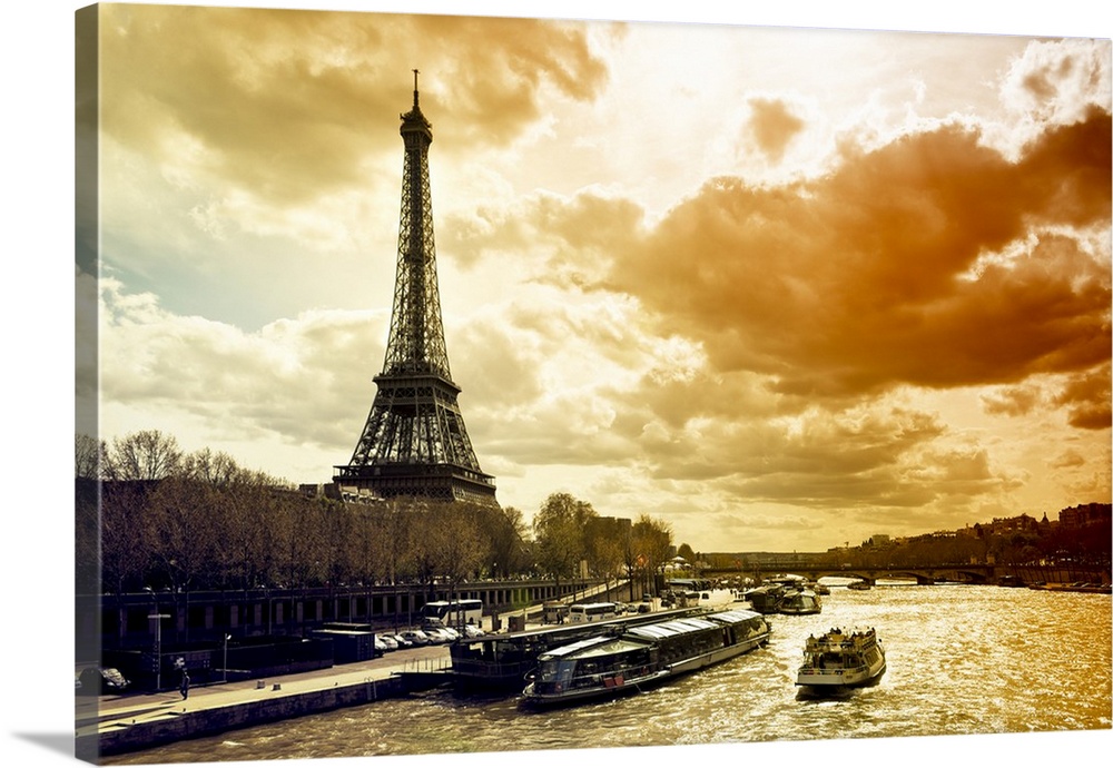 Fine art photo of the Eiffel Tower on the edge of the Seine River with dramatic lighting from the setting sun.