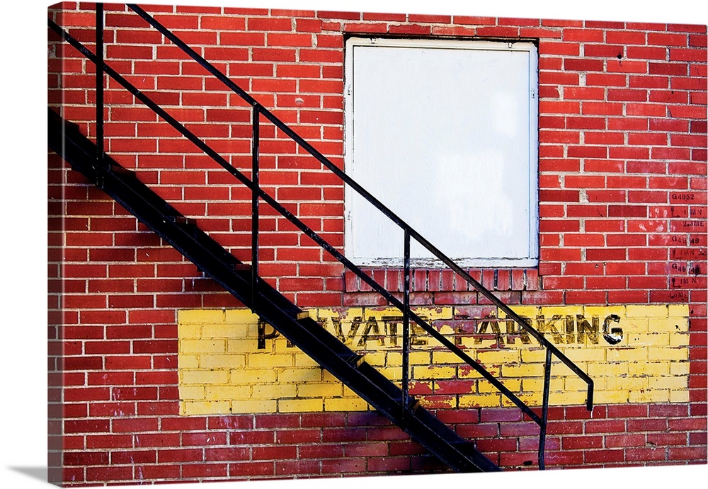 A notice of private parking is painted on a brick wall with metal fire escape stairs.