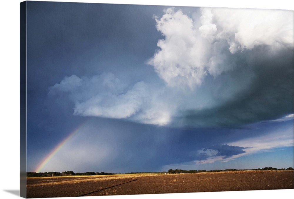 Photograph of a prairie landscape with a rainbow formed underneath dark clouds.