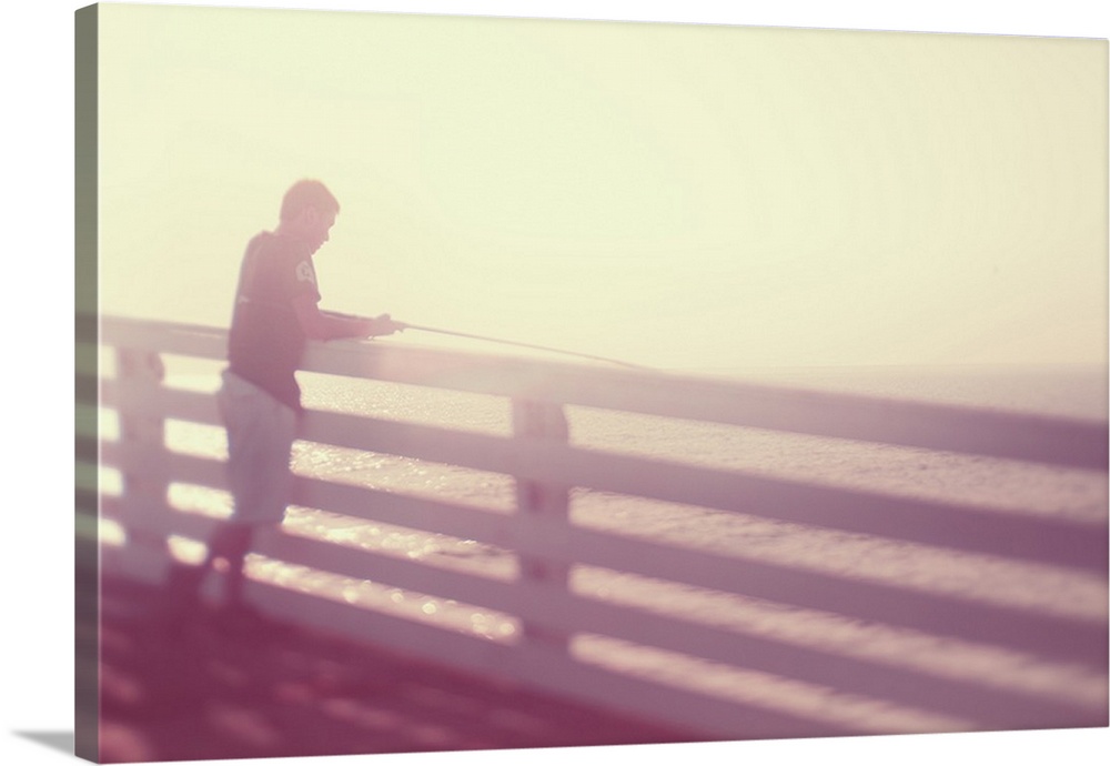 Pictorialist photo of a person fishing from the pier in the sunshine in pink hues.