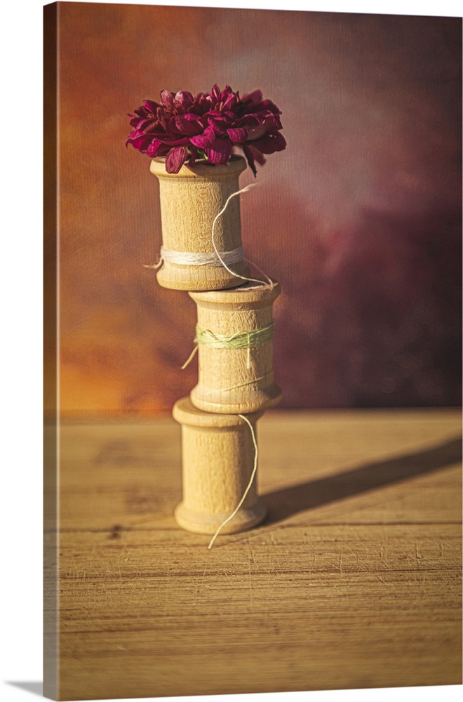 A stack of almost empty wooden thread spools with a flower on top.