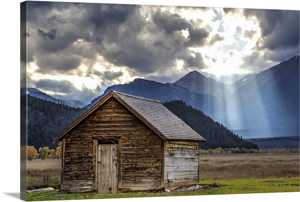 Rays of sunlight shining through the clouds over an old barn in the Grand Teton region, Wyoming.