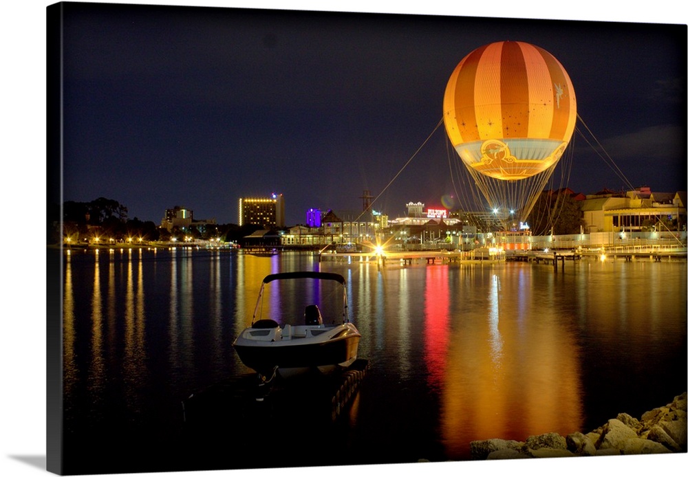 A hot air balloon glowing against the night sky over a lake.