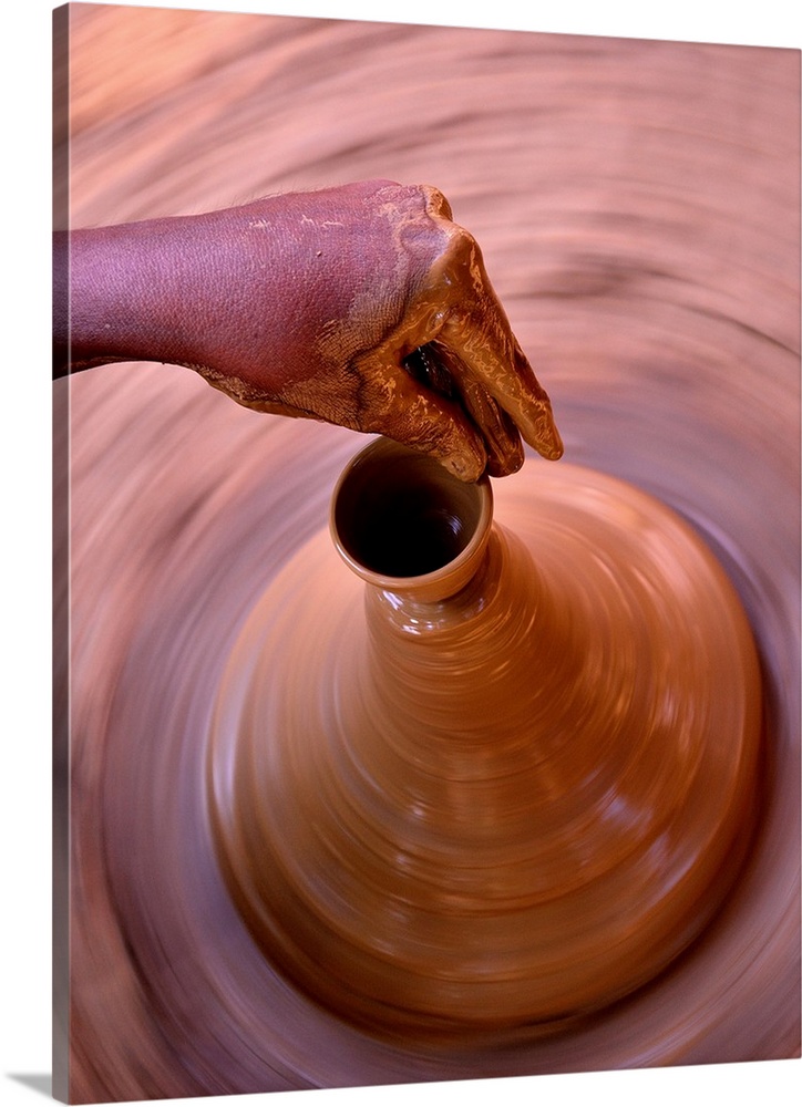 A potter sculpts the spout of a clay vessel as it spins on a pottery wheel.