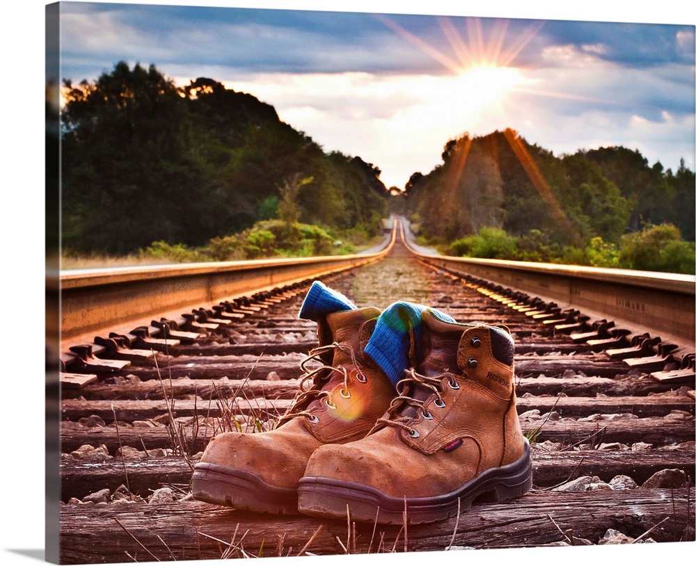 An well-worn pair of work boots in the center of railroad tracks.