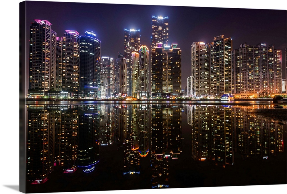 The city of Busan, South Korea, lit up at night, reflected in the water.