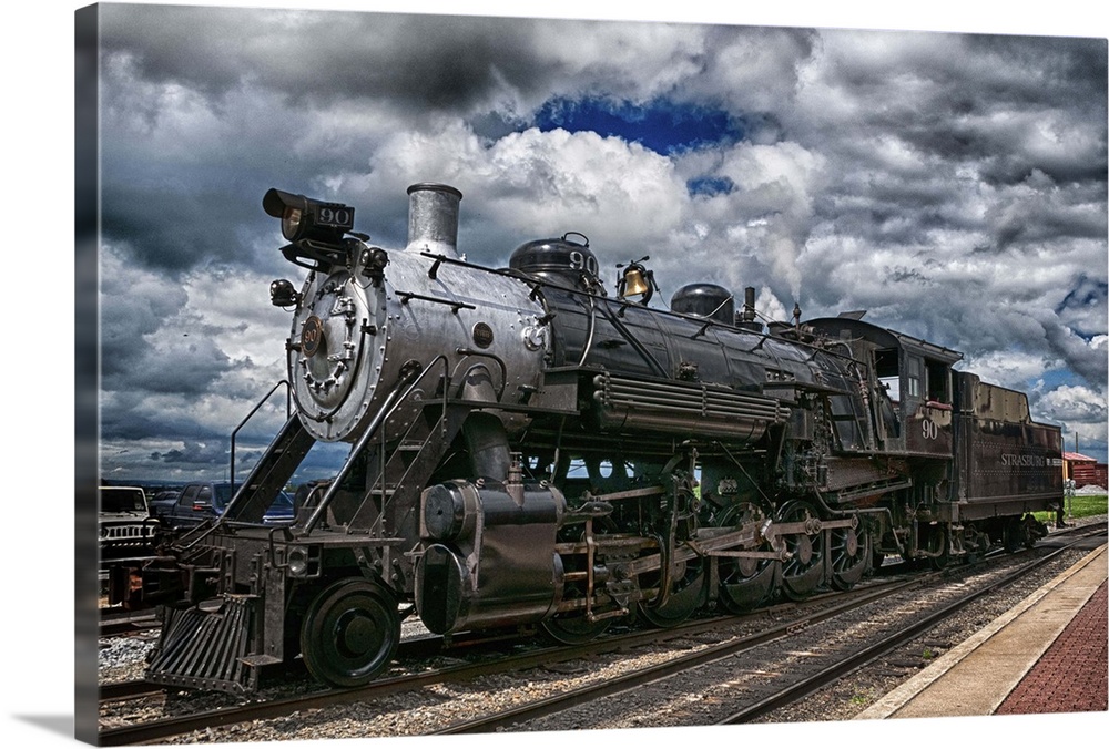 Photograph of an old steam engine sitting on train train under a dramatic cloudy sky.