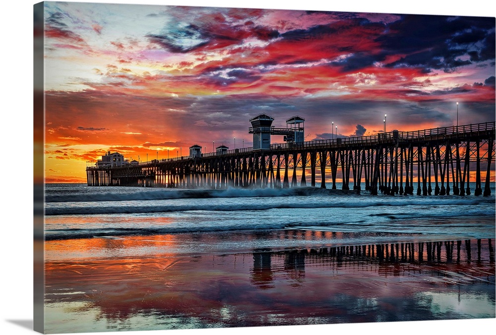The Oceanside Pier is silhouetted as sunset turns the reflected clouds from yellow to pink to gun metal grey, and finally ...
