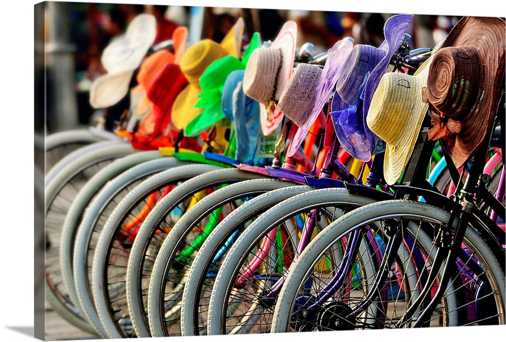 A row of bicycles with rainbow hats hanging on the handlebars.