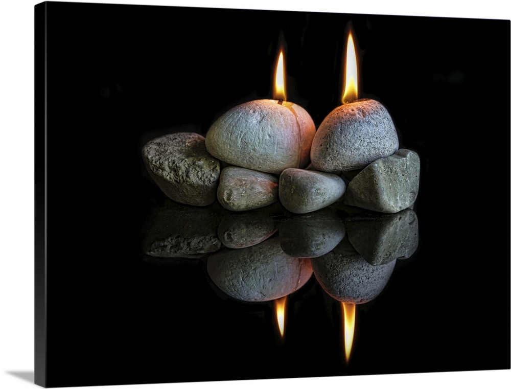 Two lit candles shaped like stones resting on rocks, with their reflection below.