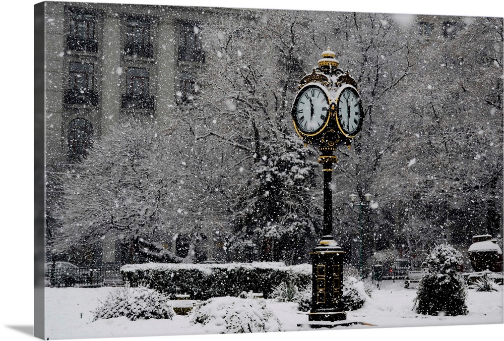 A large clock standing in a park while snow falls around it.
