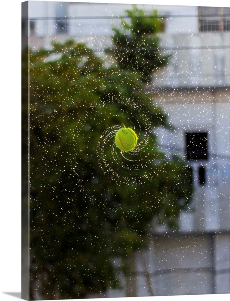 Photograph of a tennis ball spinning with water streaming off it.