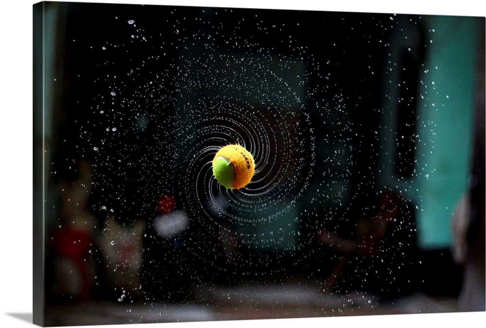 Dynamic photograph of a thrown tennis ball in a spinning motion with water spraying off it.