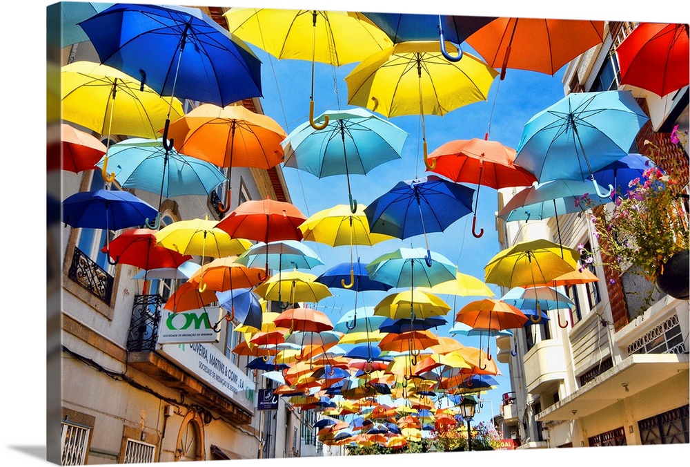 Colorful umbrellas hanging over a walkway in a village.