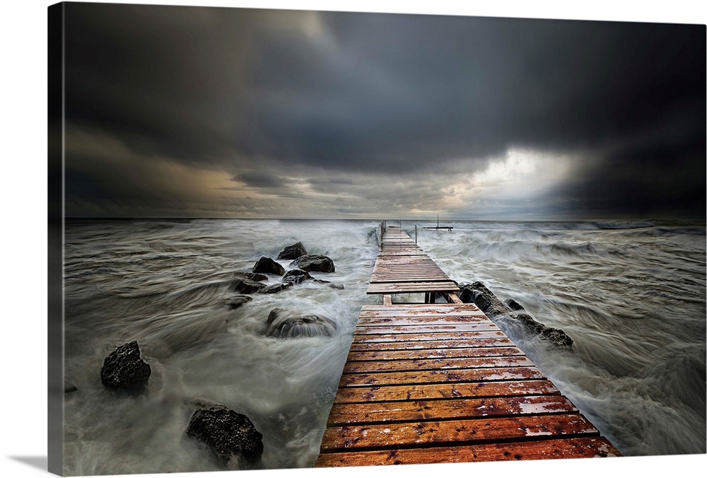 A wooden pier stretching into the sea under dark storm clouds.