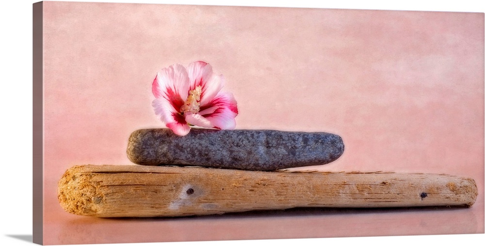 Decorative artwork that has a plank of wood with a stone on top of it and a hibiscus flower on top of the stone.