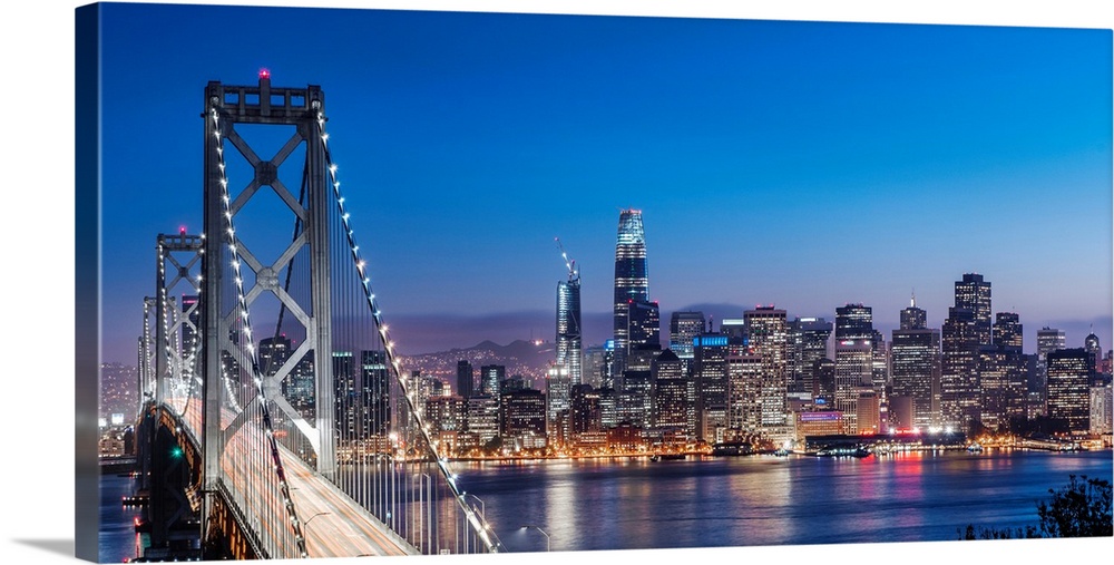 Photograph of the Bay Bridge and the San Francisco skyline lit up at dusk.