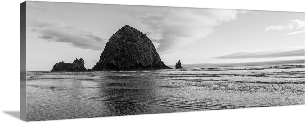 Black and white panoramic photograph of Haystack Rock with rippling waters.