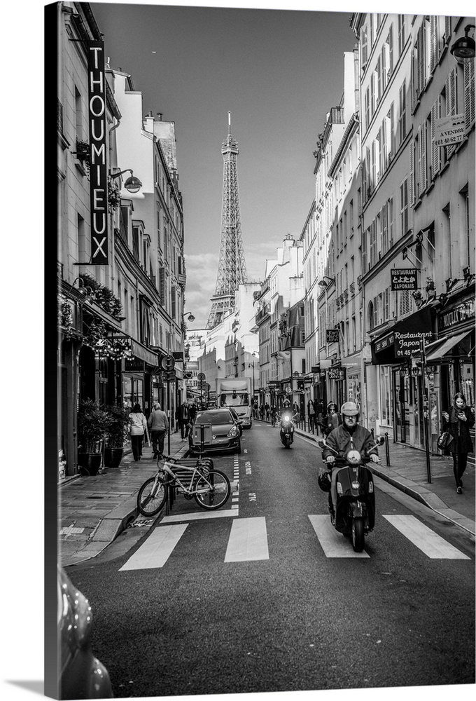 Black and white photograph of a street view in Paris with the Eiffel Tower in the background and a person on a moped in th...