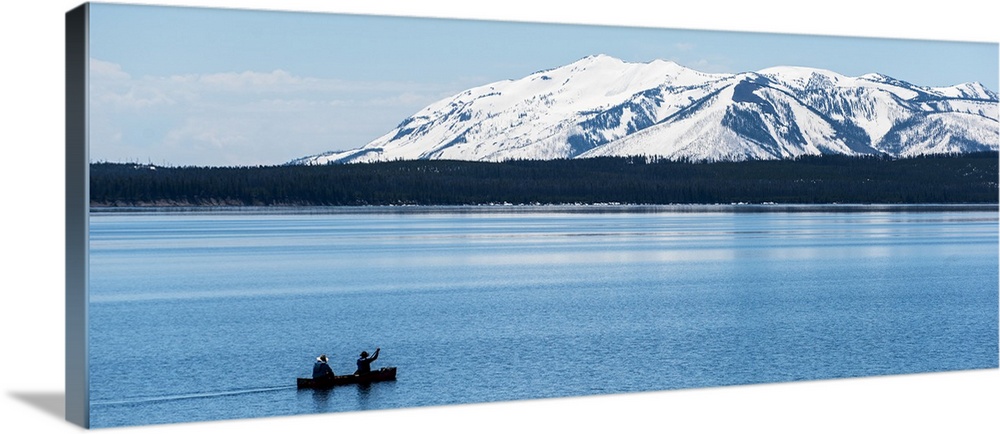 Two people canoeing on Jackson Lake with the snow covered Grand Teton mountains in the background.