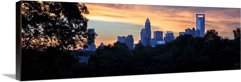 The city of Charlotte, North Carolina at sunset with a forest of trees in the foreground.