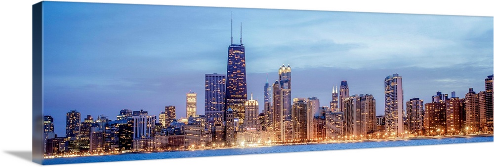 Panoramic view of the Chicago city skyline illuminated in the early evening, seen from the edge of Lake Michigan.