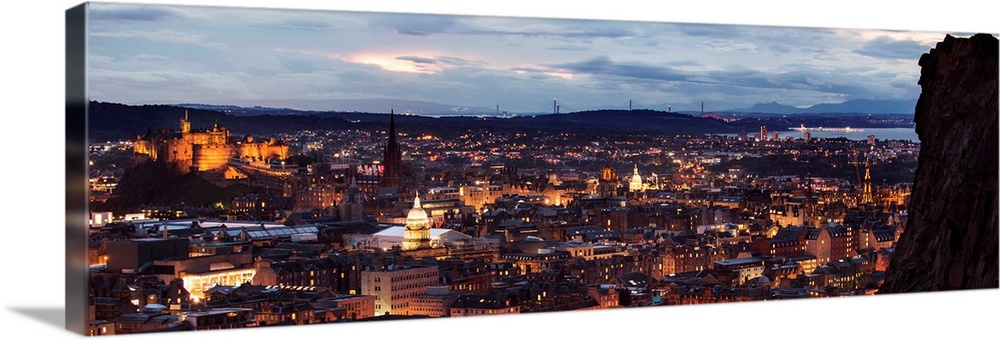 Panoramic photograph of the city of Edinburgh, Scotland lit up at sunset with a view from Holyrood Park.