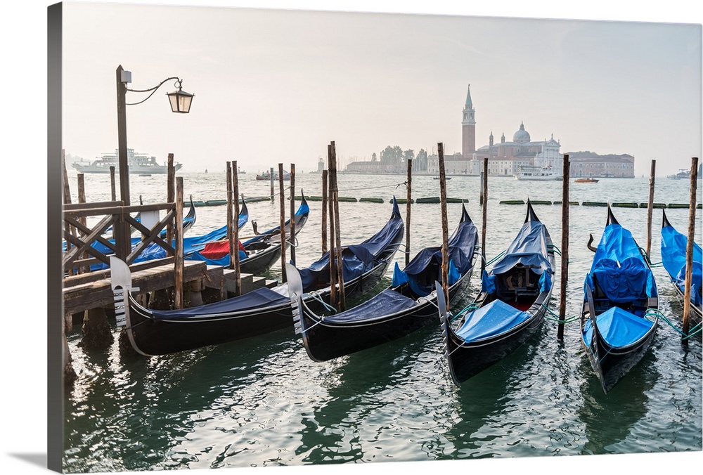 Photograph of gondolas lined up in a row with St. Mark's Square (Piazza San Marco) in the background.