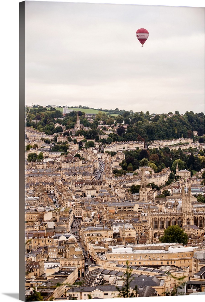 Photograph of a red and white hot air balloon flying over the city of Bath in England, UK.
