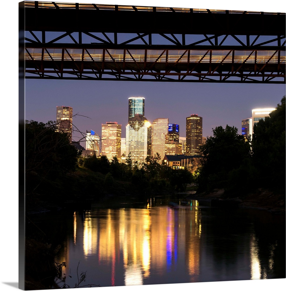 Square photograph of the Houston TX skyline at night reflecting into the Buffalo Bayou with the Rosemont Pedestrian Bridge...