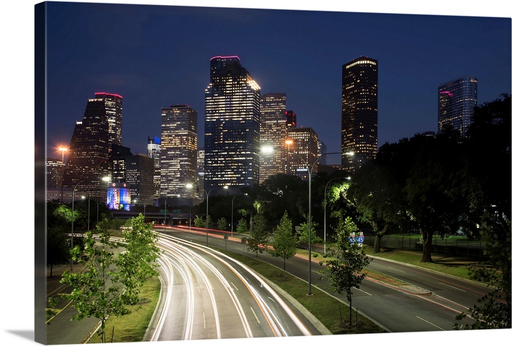 Long exposure photograph of the Houston TX skyline at night from the highway with red and white light trails on the road.