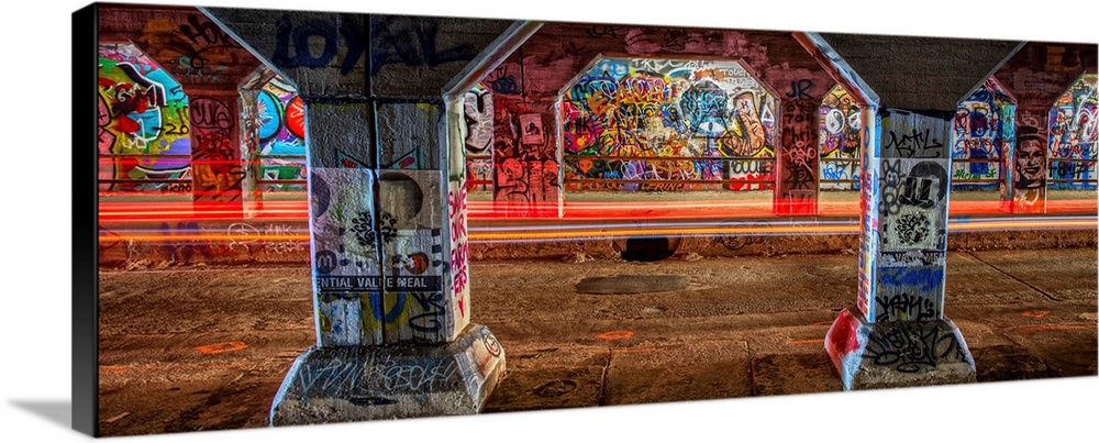 Light trails from passing cars create a red glow, lighting up the graffiti on the walls and columsn in the Krog Street Tun...