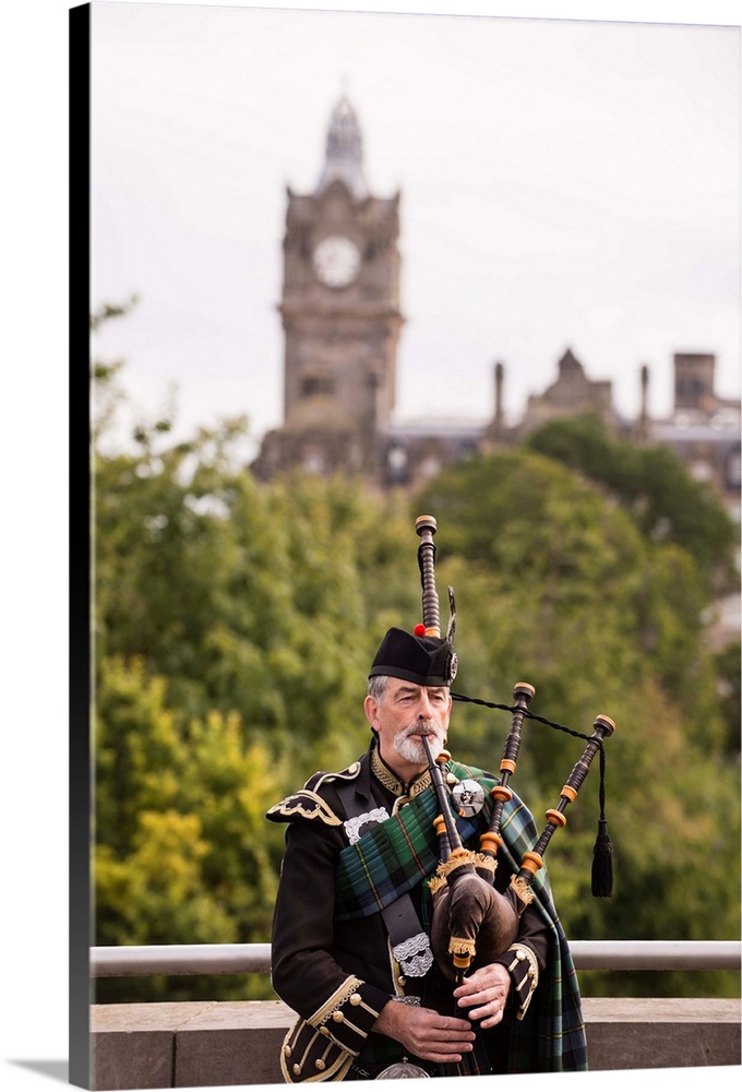 Photograph of a man playing the bagpipes in Edinburgh with the clock tower blurred out in the background.