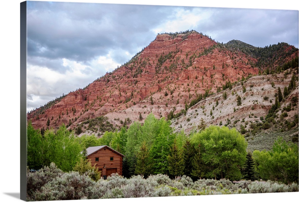 Photo of a wood cabin nestled with trees under a mountain cliffside in Colorado.