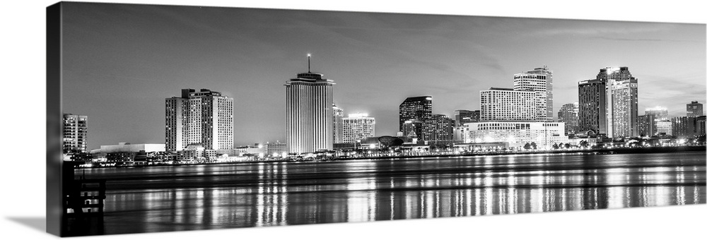 Panoramic photograph of the New Orleans skyline lit up at night with reflecting bands onto the Mississippi River.