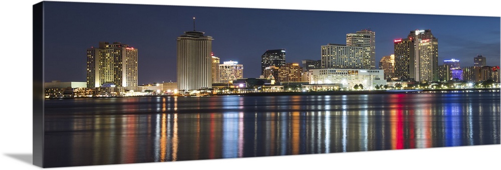 Panoramic photograph of the New Orleans skyline lit up at night and reflecting colorful bands onto the Mississippi River.